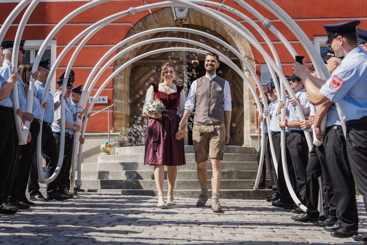 Carina und Mario in Tracht verlassen das Standesamt Burglengenfeld durch ein Spalier der Freiwilligen Feuerwehr mit Schlauchbögen und Seifenblasen